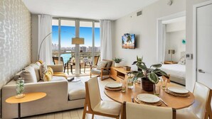 A modern hotel room with a large window offering a city view, a dining area, and a cozy seating area with a sofa and chairs. - Beautiful Views + Amazing Pool+ Beach access (Hallandale Beach)