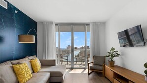 Un soggiorno moderno con divano, poltrone, televisore e un balcone con vista sulla città.