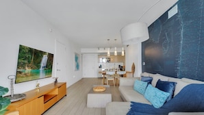 Ein modernes Wohnzimmer mit großem Flachbildfernseher, einer Holzunterhaltungsecke, einer Couch mit gemusterten Kissen und einem Essbereich im Hintergrund.
