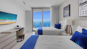 A modern hotel room with two beds, a desk, and a large window offering a sea view. - Bright & Spacious 2BR w/Balcony (Hollywood)
