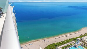 A high vantage point view of a beach with a clear sky, a swimming pool, and a beach area with umbrellas. - Bright & Spacious 2BR w/Balcony (Hollywood)