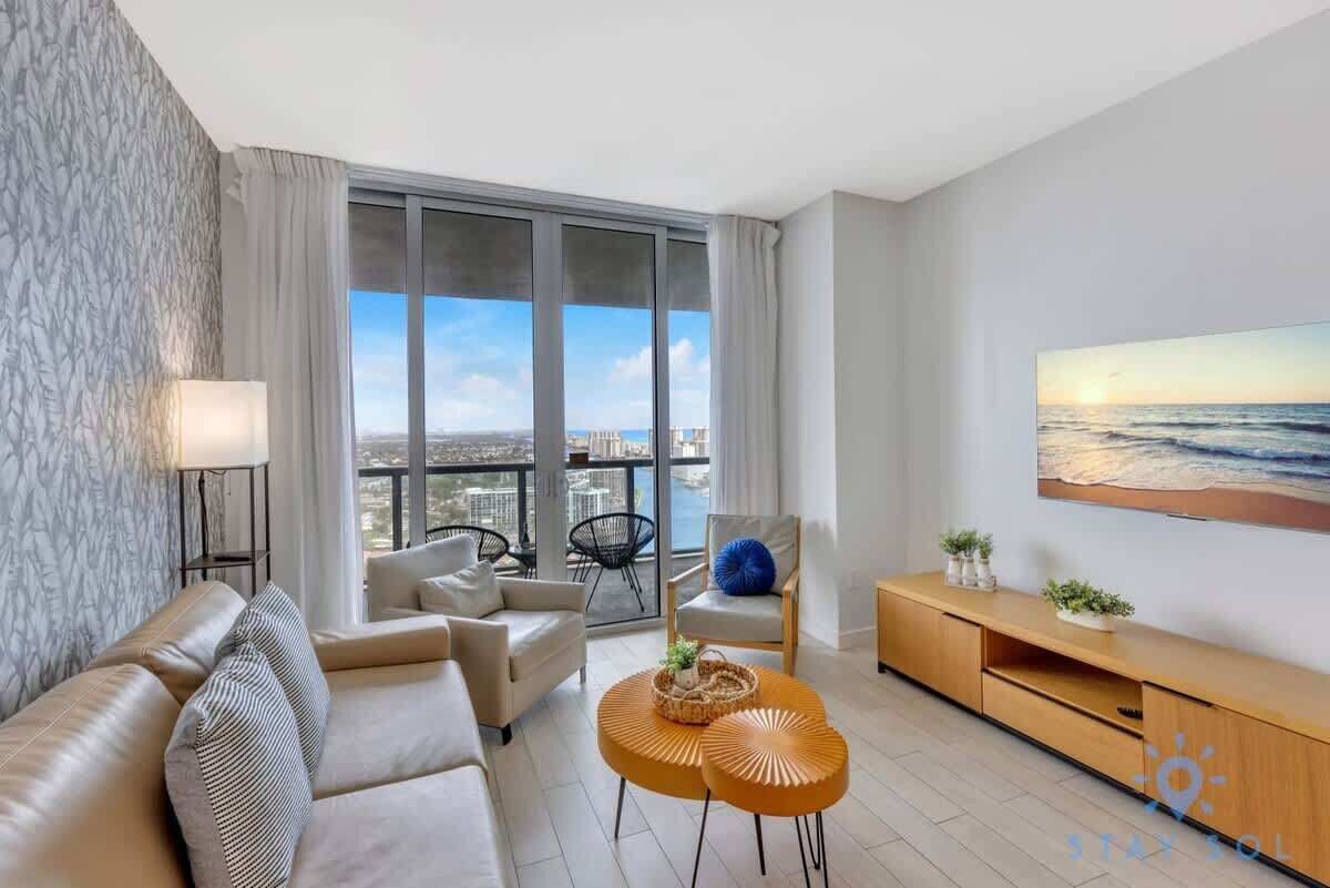 Ein modernes Wohnzimmer mit einer Couch, zwei runden Couchtischen, einem Fernseher und einem großen Fenster mit Stadtblick.