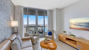 A modern living room with a sofa, two round coffee tables, a TV, and a large window with a view of the city.
