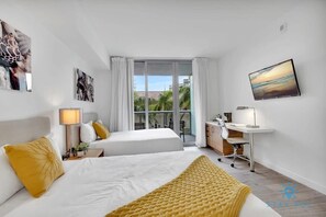 Habitación de hotel con dos camas, un escritorio, una silla y un amplio ventanal con vista a palmeras.