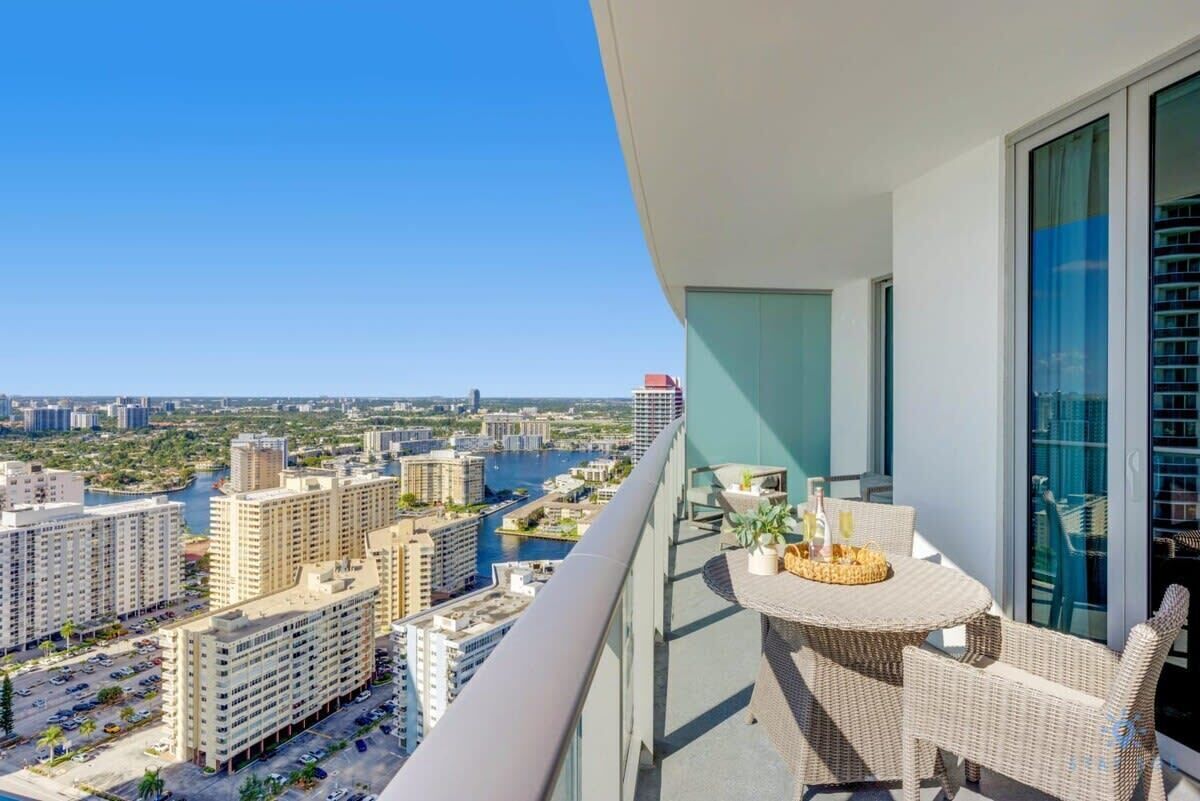 Un balcón con mobiliario de mimbre, una mesa con bebidas y vistas a la ciudad.