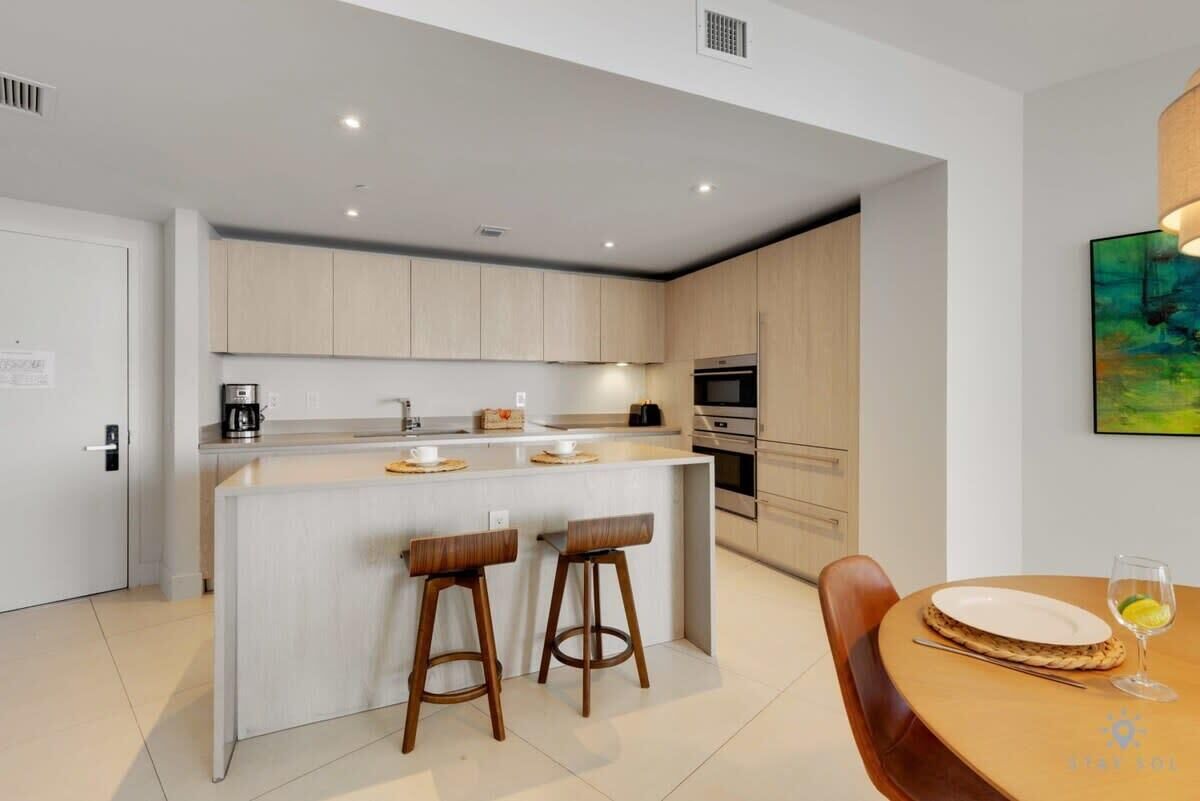 A modern kitchen with a central island, bar stools, and a dining table with a glass of wine.