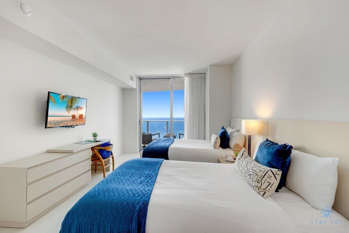 Una habitación de hotel moderna con una cama grande, un escritorio, un televisor y un balcón con vista al mar.