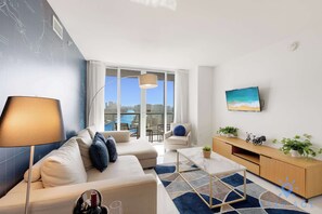 Ein modernes Wohnzimmer mit Sofa, Couchtisch und Fernseher. Ein Balkon bietet Blick auf die Stadt.