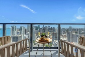 Ein Hotelzimmer in einem Hochhaus mit Blick auf die Stadt, ein kleiner runder Tisch mit einer Flasche und einem Glas sowie zwei Stühle.