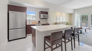 A modern kitchen with a central island, stainless steel appliances, and a dining area with dark wooden chairs. - New in Miami! 1BR -Stylish Apartment (Doral)