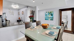 A modern dining area with a glass table, chairs, and a kitchen in the background. - Amazing Apt w/Ocean View + Pool & Gym (Miami)