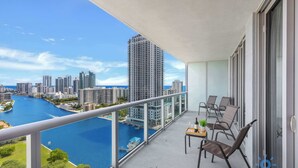 Varanda com vista para um rio e o horizonte urbano, equipada com cadeiras e uma mesa.