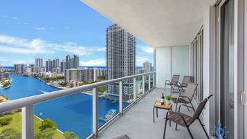 Varanda com vista para um rio e o horizonte urbano, equipada com cadeiras e uma mesa.