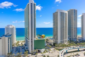 A high-rise hotel with a rooftop pool, a parking area, and a view of the ocean. - Beautiful 2BR Apt w/Ocean View + Pool + Amenities (Hollywood)
