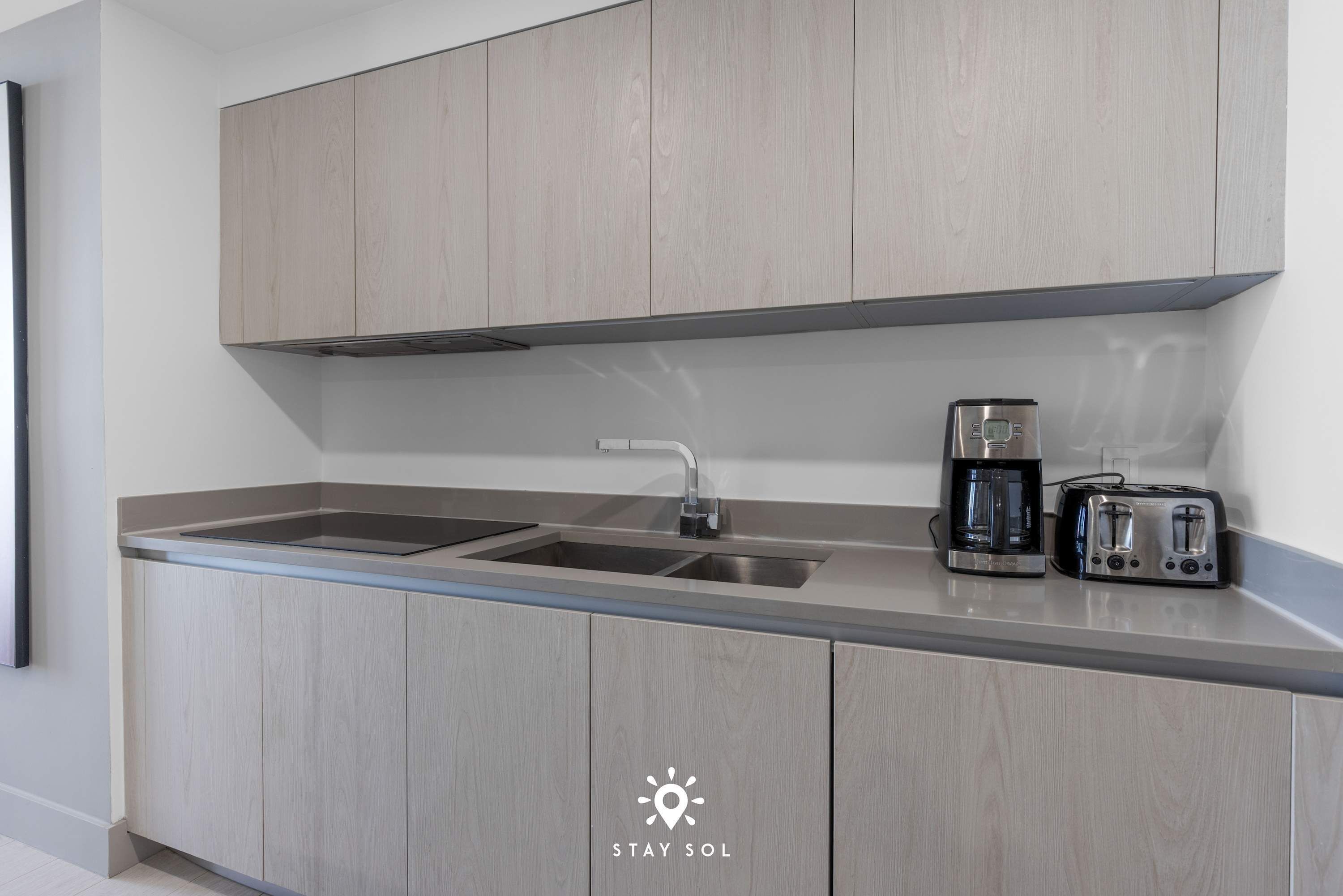 A modern kitchen with light wood cabinets, a stainless steel sink, a coffee maker, and a toaster.