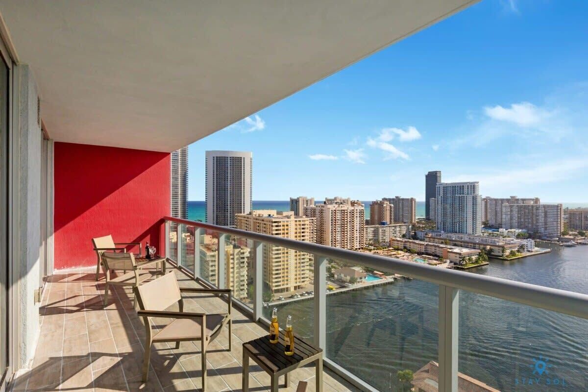 A balcony with a red wall, a view of a city skyline, and a body of water.