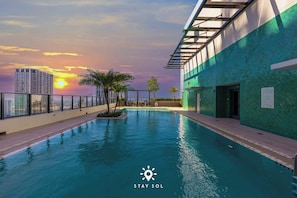 Ein Pool mit Sonnenuntergangsblick, einer Glasreling und einem Gebäude mit grüner Fassade.