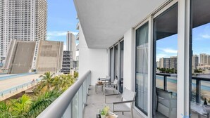 Un balcón con mesa lista para comer, ventanas amplias y vista a la ciudad.