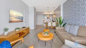 Een moderne woonkamer met een bank, een salontafel en een televisie op een houten console. Achtergrond is een keuken met een eethoek.