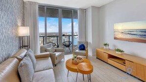 Een moderne woonkamer met een bank, twee ronde salontafels, een televisie en een groot raam met uitzicht op de stad.