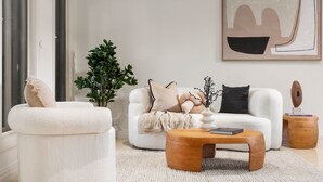 A modern living room with a white sofa, a round wooden coffee table, and a potted plant.