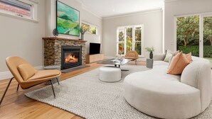 A modern living room with a fireplace, comfortable seating, and large windows.