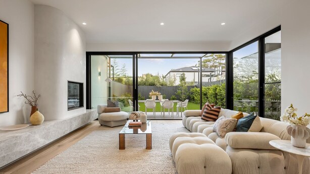 A modern living room with a large sofa, a coffee table, and a view of the backyard through large windows.