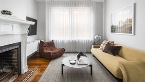 A living room with a fireplace, a sofa, a coffee table, and a window with sheer curtains.