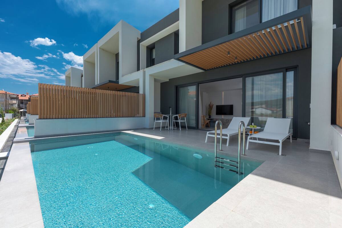 Et moderne poolområde med et klart pool, hvide liggestole og et overdækket siddeområde.