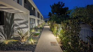 A pathway flanked by modern buildings, a well-maintained garden with various plants, and a blue fence. - Viridian Exclusive Villas (Sithonia)