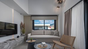 A modern living room with a sofa, a flat-screen TV, two coffee tables, a wicker chair, and a large window with curtains. - Viridian Exclusive Villas (Sithonia)