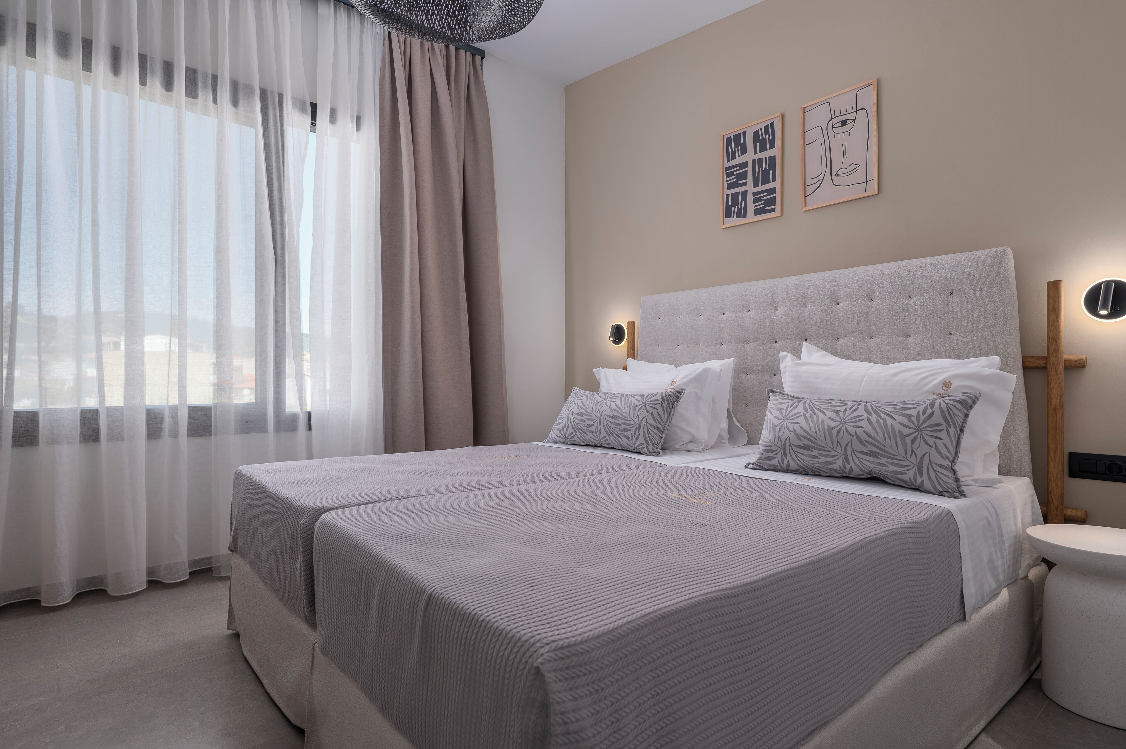 A modern hotel room with a large bed, two bedside tables, a nightstand, and a window with sheer curtains.