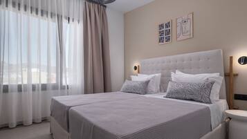 A modern hotel room with a large bed, two bedside tables, a nightstand, and a window with sheer curtains.