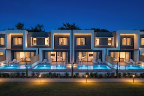 A modern multi-story building with a swimming pool, outdoor seating, and a well-lit entrance.