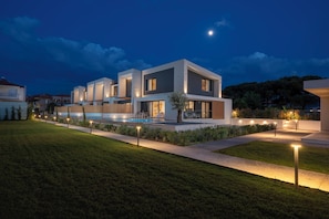 A modern two-story house with a swimming pool, surrounded by a well-maintained lawn and pathway.