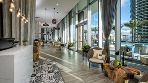 A modern hotel lobby with large windows, a pool view, and a mix of seating areas. - Beautiful Apt w/ Amazing Pool and Private Balcony (Hollywood)