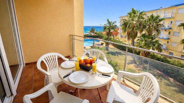 Een balkon met een tafel gedekt voor twee personen, inclusief borden, bestek en een fruitschaal met sinaasappels en sap.