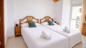 Een hotelkamer met twee enkele bedden, houten hoofdeinden, wit beddengoed en een raam met uitzicht.