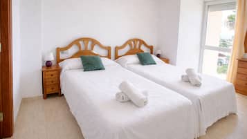 A hotel room with two single beds, wooden headboards, white bedding, and a window with a view.