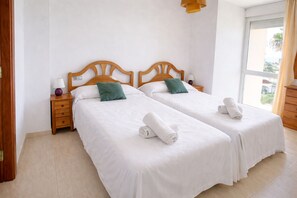Ein Hotelzimmer mit zwei Einzelbetten, Holz-Kopfteilen, weißer Bettwäsche und einem Fenster mit Aussicht.