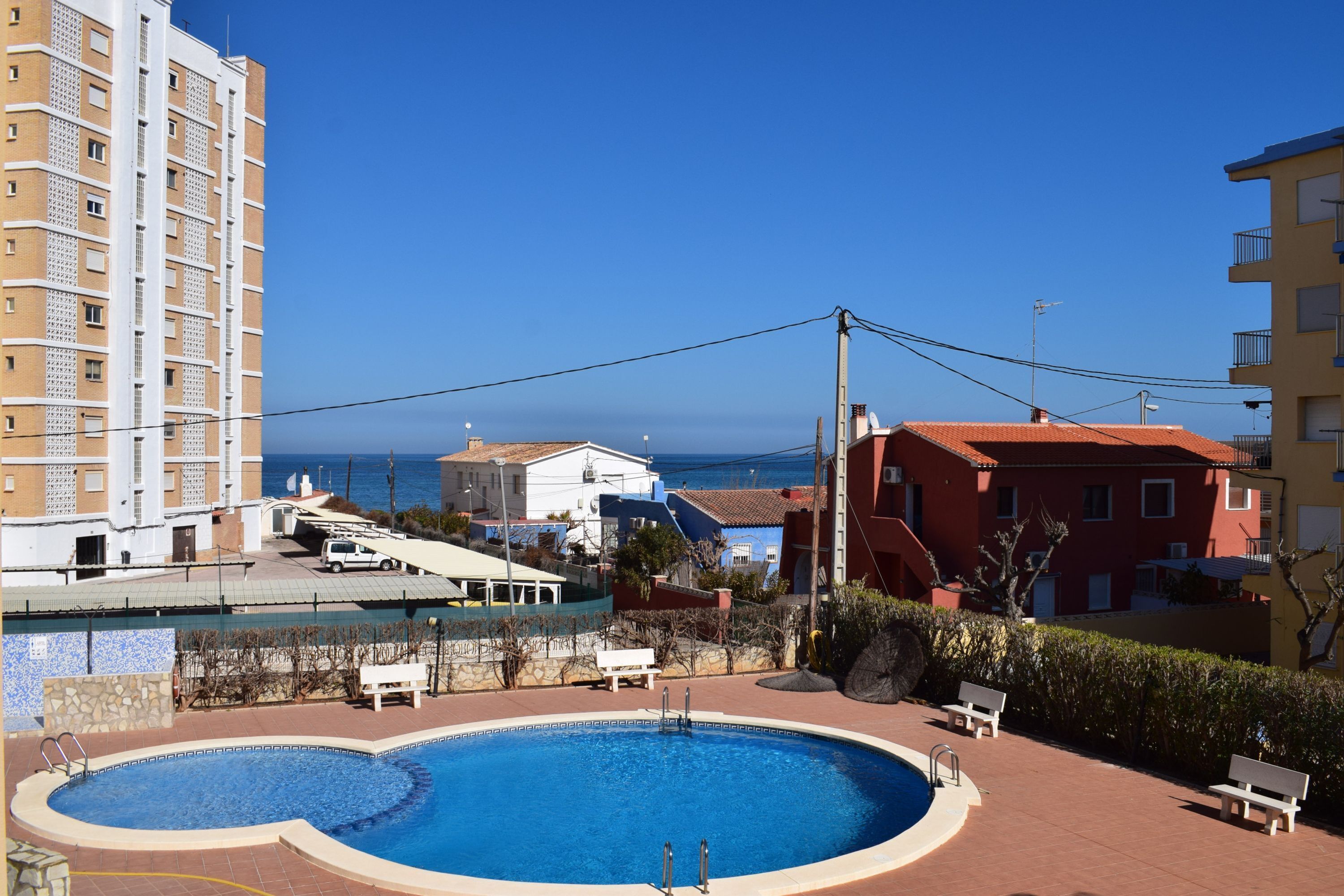 Piscina com design curvo, cercada por um espaço pavimentado com bancos e um muro de pedra.