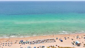 Une plage bordée de rangées de chaises longues et de parasols, avec une tour de surveillance et l’océan en toile de fond.