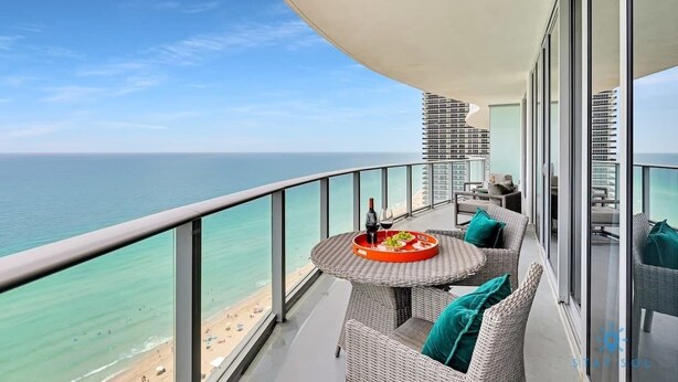 Un balcon avec une table ronde, des meubles en osier et une vue sur la plage et l’océan.