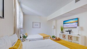 Habitación de hotel con dos camas, un televisor, un escritorio con lámpara y un cuadro en la pared.