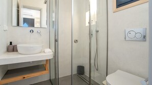 Un baño moderno con cabina de ducha de vidrio, un lavabo blanco y un inodoro.