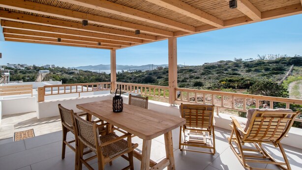 Terraza de madera con mesa y sillas, con vistas a un paisaje montañoso.