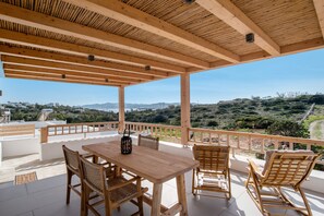 Terraza de madera con mesa y sillas, con vistas a un paisaje montañoso.