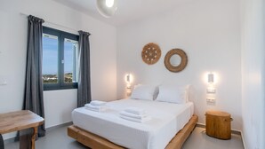 Un dormitorio con cama de madera, ropa de cama blanca, vistas por una ventana y luces fijadas a la pared.