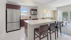 Een moderne keuken met een groot eiland, roestvrijstalen apparatuur en een eethoek met donkerhouten stoelen.
