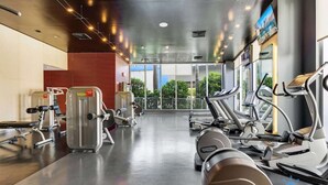 A gym with treadmills, weight machines, and a large window offering a view of greenery and buildings. - Beachside Stay | Infinite View | Balcony | Miami (Hallandale Beach)